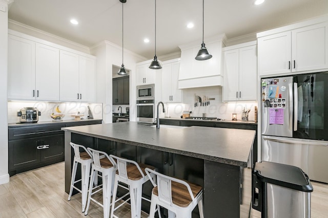 kitchen with stainless steel appliances, dark countertops, a kitchen island with sink, and white cabinetry