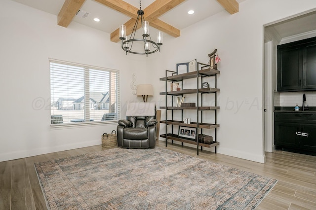 living area featuring light wood-style floors, beamed ceiling, baseboards, and an inviting chandelier