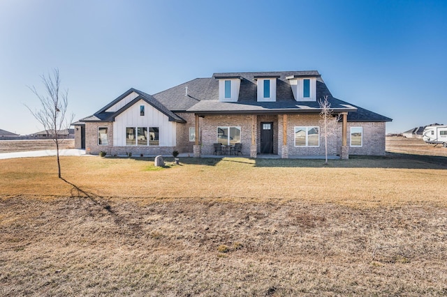 view of front facade featuring a front lawn, roof with shingles, board and batten siding, and brick siding