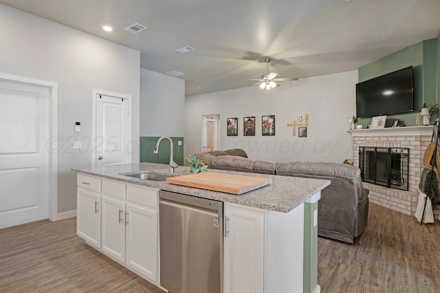 kitchen with an island with sink, a brick fireplace, dishwasher, white cabinets, and sink