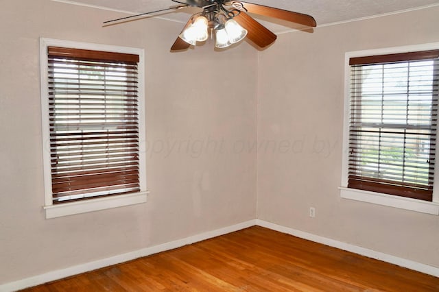 spare room featuring plenty of natural light, baseboards, wood finished floors, a ceiling fan, and ornamental molding