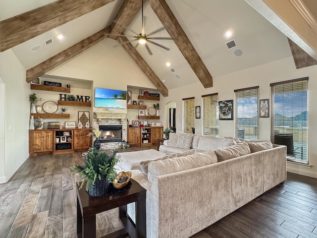 living room featuring ceiling fan, high vaulted ceiling, dark hardwood / wood-style floors, a stone fireplace, and beamed ceiling