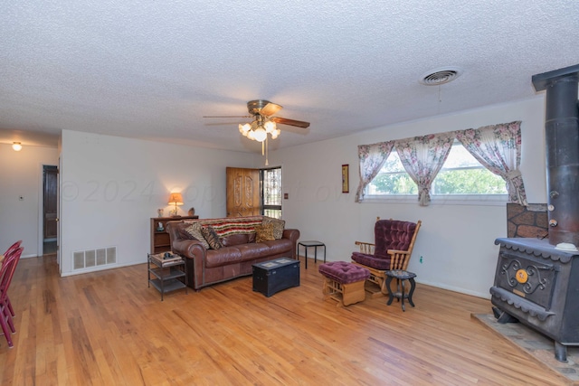 living room featuring ceiling fan, wood-type flooring, a textured ceiling, and a wood stove