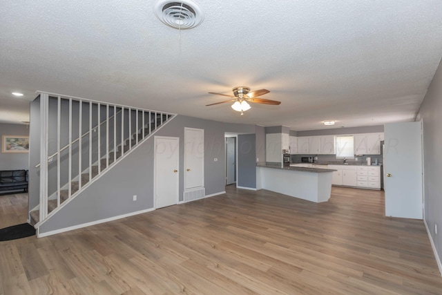 unfurnished living room with sink, light wood-type flooring, a textured ceiling, and ceiling fan