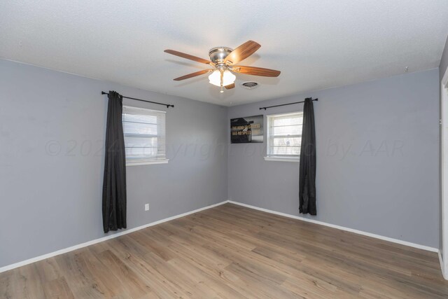 empty room featuring a wealth of natural light, ceiling fan, and light wood-type flooring