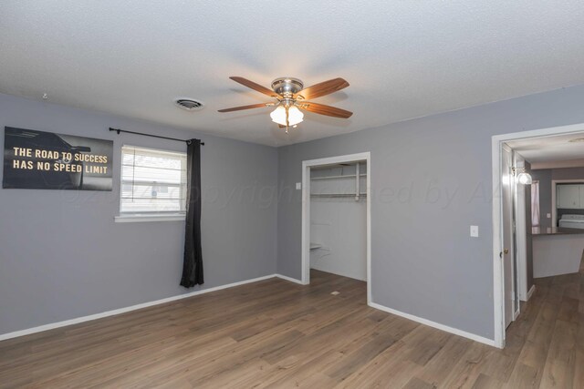 unfurnished bedroom with a textured ceiling, wood-type flooring, ceiling fan, and a closet