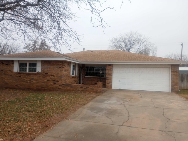 ranch-style home featuring a garage, concrete driveway, brick siding, and roof with shingles