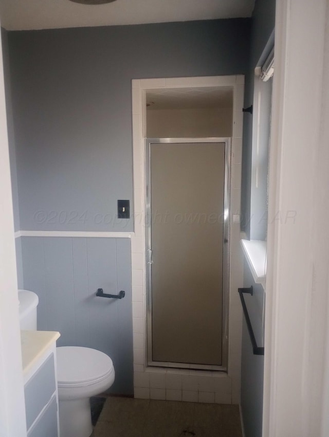 bathroom with toilet, a wainscoted wall, vanity, tile walls, and a stall shower