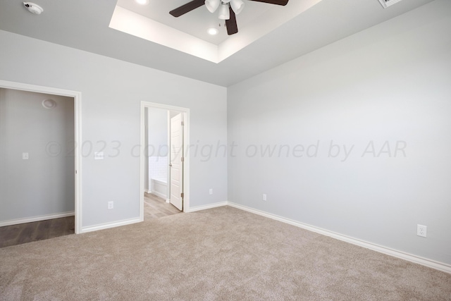 unfurnished bedroom with ceiling fan, light colored carpet, a raised ceiling, and ensuite bath