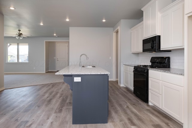 kitchen with sink, white cabinets, black appliances, light stone countertops, and a center island with sink