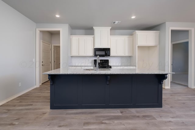 kitchen featuring light stone counters, sink, an island with sink, and white cabinets