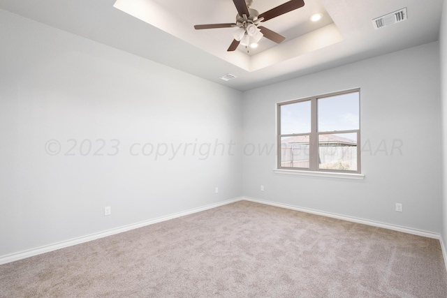 spare room with light carpet, ceiling fan, and a tray ceiling