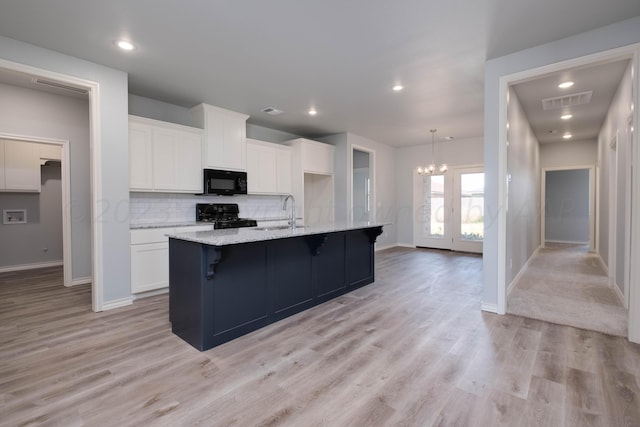 kitchen with sink, white cabinetry, tasteful backsplash, black appliances, and an island with sink