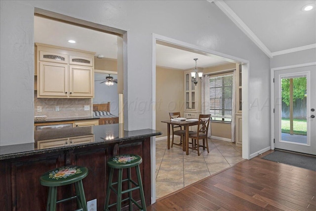7104 Old Kent Rd, Amarillo, TX 79109 - kitchen featuring vaulted ceiling, backsplash, a kitchen bar, ornamental molding, and cream cabinetry