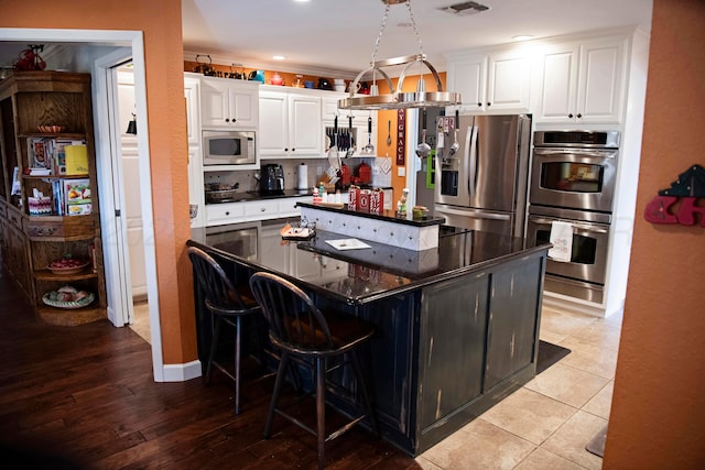 kitchen with white cabinets, stainless steel appliances, light hardwood / wood-style floors, and a breakfast bar area