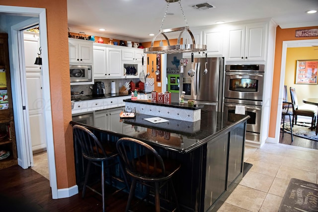 kitchen with white cabinets, a kitchen island, light tile patterned floors, and stainless steel appliances