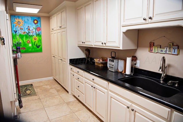 kitchen with sink, white cabinets, light tile patterned floors, and ornamental molding