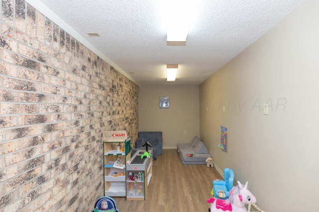 rec room featuring a textured ceiling, brick wall, wood finished floors, and baseboards