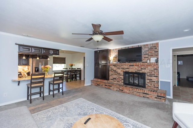 carpeted living room featuring a ceiling fan, baseboards, a fireplace, and crown molding