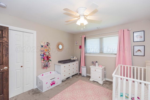 bedroom with light colored carpet, a closet, ceiling fan, a crib, and baseboards