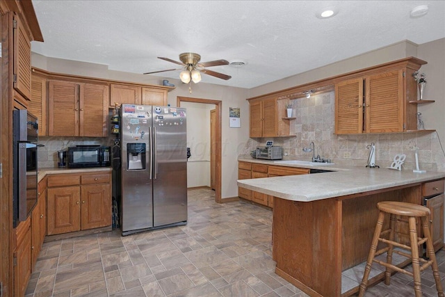 kitchen with appliances with stainless steel finishes, a sink, brown cabinetry, and ceiling fan