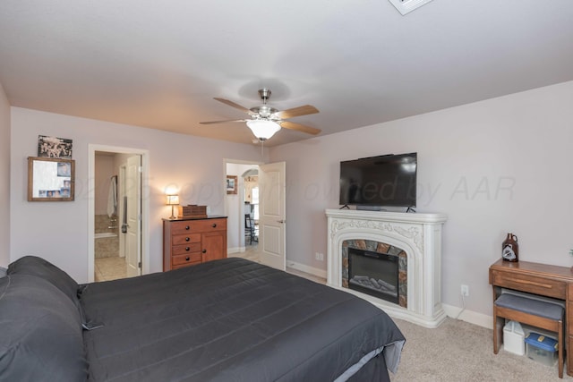 bedroom featuring baseboards, a ceiling fan, ensuite bath, carpet flooring, and a premium fireplace