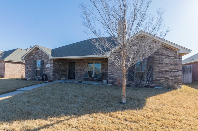 single story home with a shingled roof, a front yard, a patio area, and brick siding