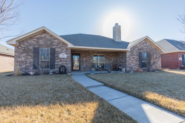 ranch-style house featuring a shingled roof, a front yard, a chimney, and brick siding