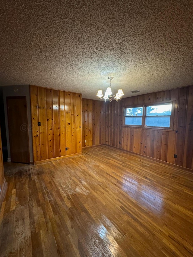 empty room featuring wood walls, wood-type flooring, and a notable chandelier