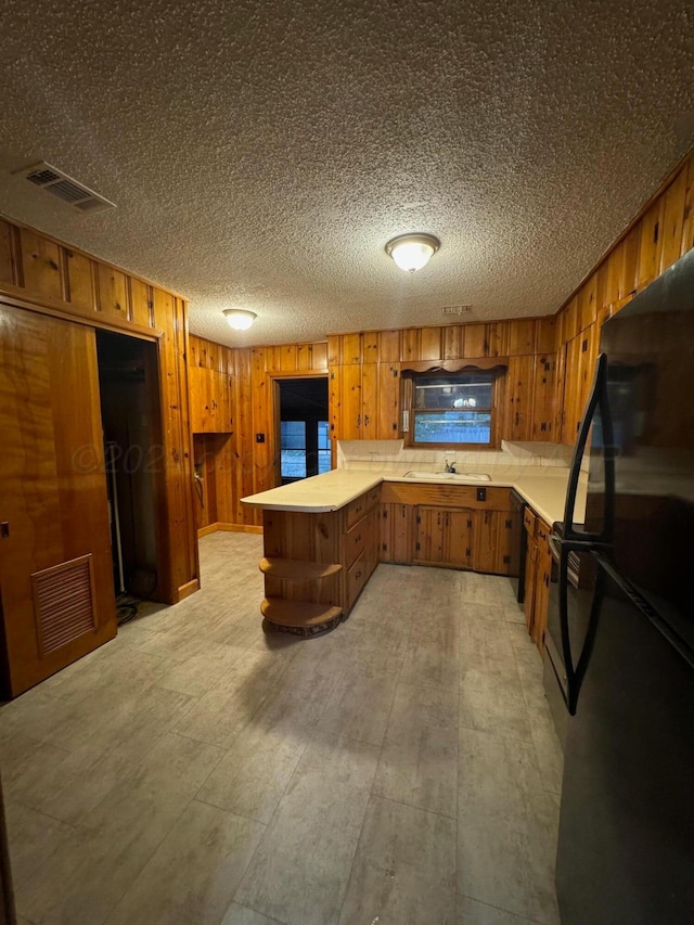 kitchen featuring wood walls, black fridge, sink, a textured ceiling, and kitchen peninsula