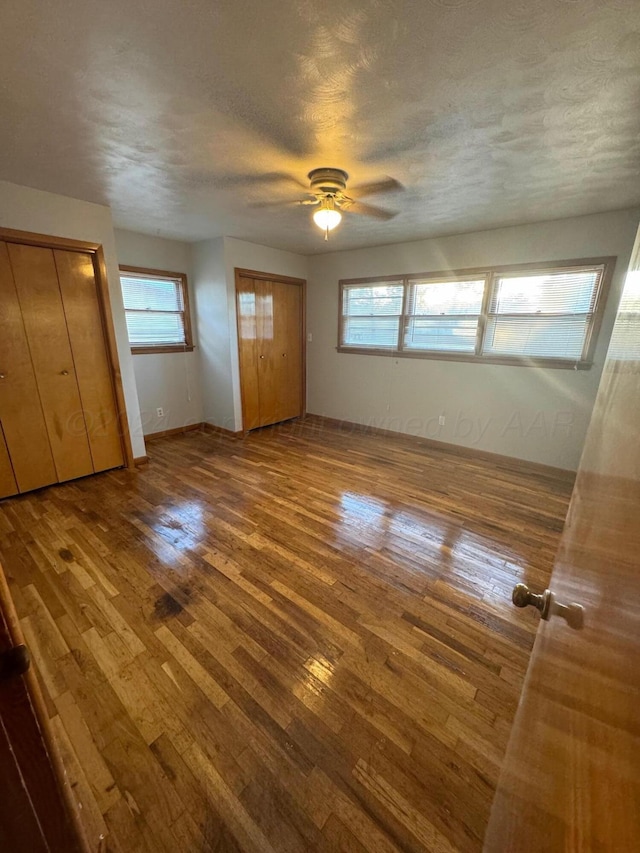 unfurnished bedroom with hardwood / wood-style floors, ceiling fan, a textured ceiling, and two closets