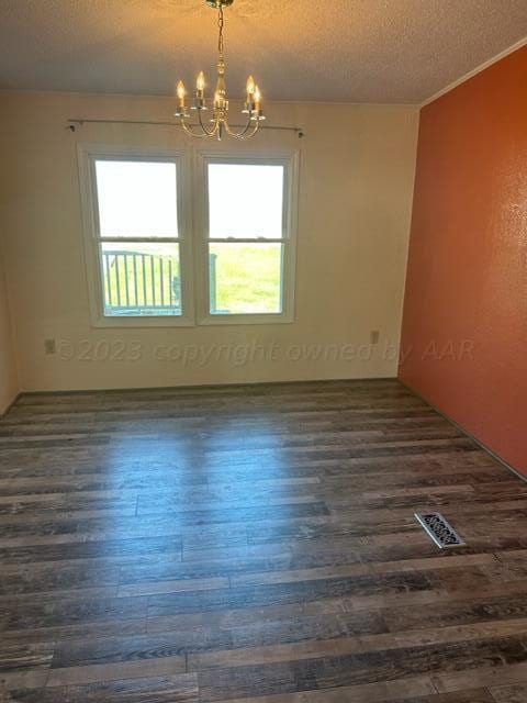 unfurnished room with a textured ceiling, dark wood-type flooring, and an inviting chandelier