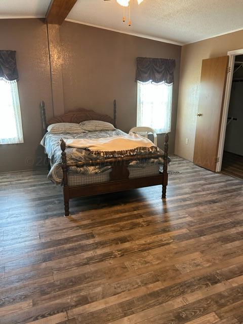 bedroom featuring beam ceiling, a walk in closet, dark hardwood / wood-style floors, and a textured ceiling