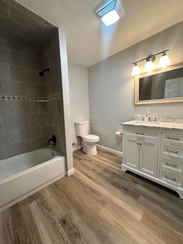 full bathroom with tiled shower / bath, vanity, wood-type flooring, and toilet