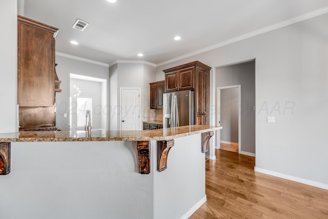 kitchen featuring a breakfast bar area, light hardwood / wood-style flooring, ornamental molding, stainless steel fridge, and kitchen peninsula