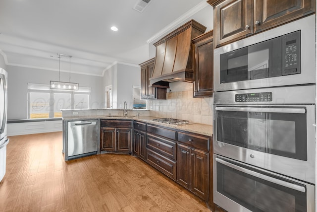 kitchen with appliances with stainless steel finishes, pendant lighting, sink, ornamental molding, and custom range hood
