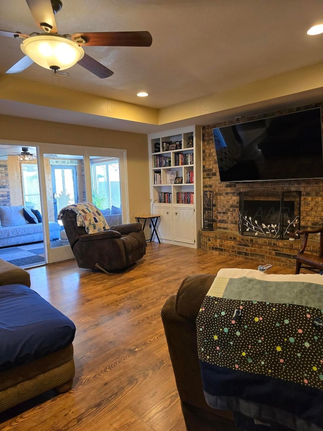 living room with a brick fireplace, wood-type flooring, and ceiling fan