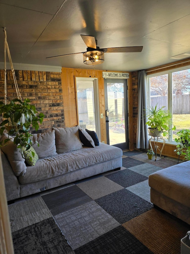 carpeted living room with ceiling fan and brick wall