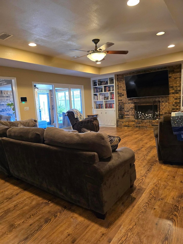 living room with a brick fireplace, hardwood / wood-style floors, ceiling fan, and built in shelves