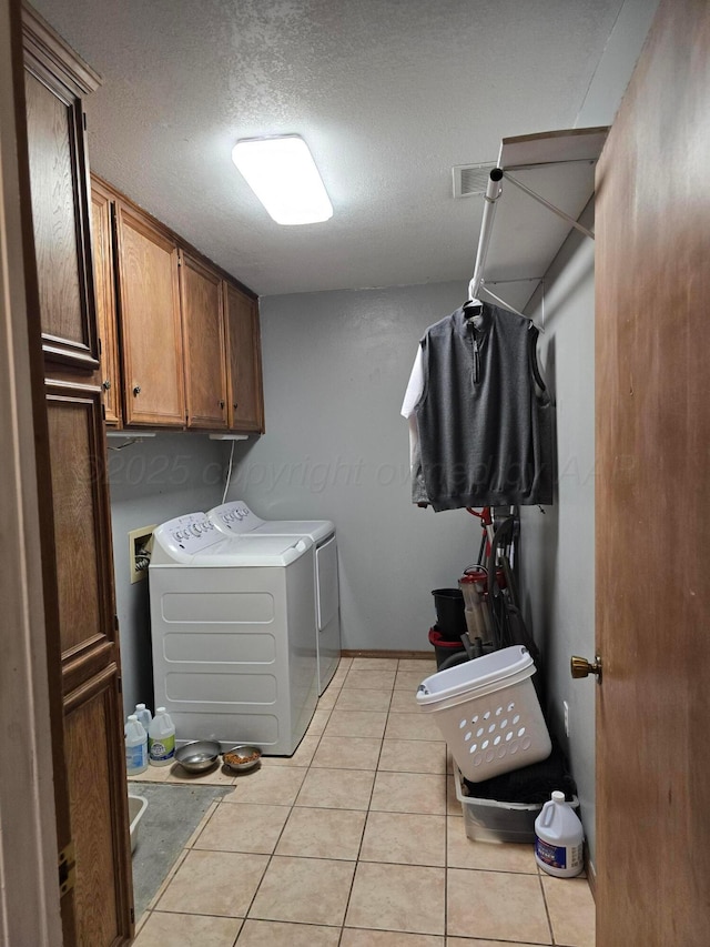 laundry room with light tile patterned floors, a textured ceiling, cabinets, and washing machine and clothes dryer