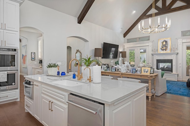 kitchen with stainless steel appliances, white cabinetry, light stone countertops, a kitchen island with sink, and dark hardwood / wood-style flooring