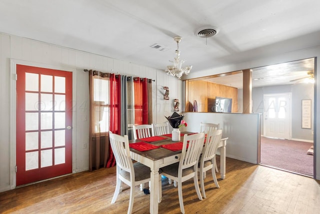 dining area with wood walls, hardwood / wood-style floors, and a notable chandelier