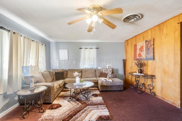 carpeted living room with wood walls and ceiling fan