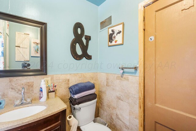 bathroom with toilet, vanity, and tile walls