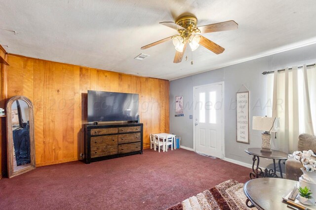 living room featuring wood walls, ceiling fan, and dark carpet