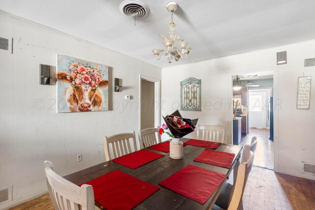 dining space with ceiling fan with notable chandelier and hardwood / wood-style flooring