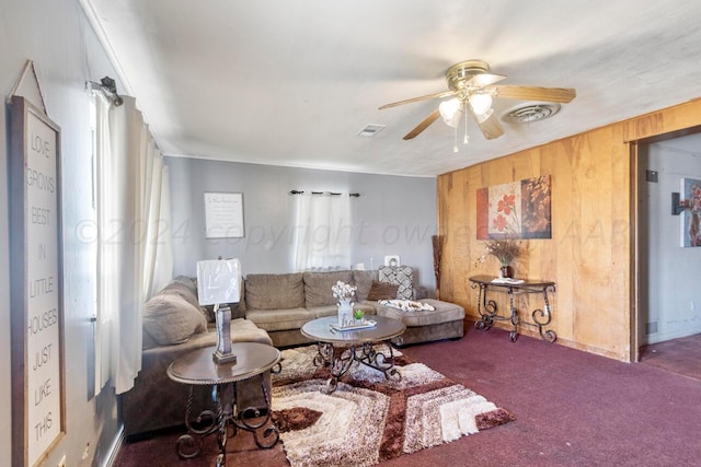 carpeted living room featuring wood walls and ceiling fan