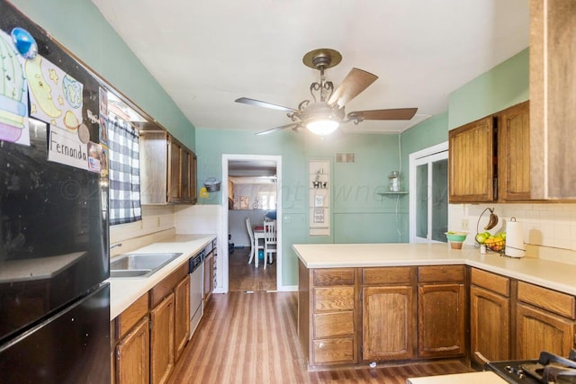 kitchen with black refrigerator, kitchen peninsula, hardwood / wood-style flooring, tasteful backsplash, and sink