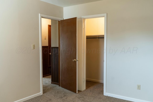 unfurnished bedroom with a spacious closet, light colored carpet, and a closet