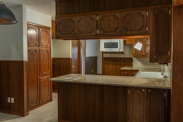 kitchen featuring sink, backsplash, wooden walls, and kitchen peninsula